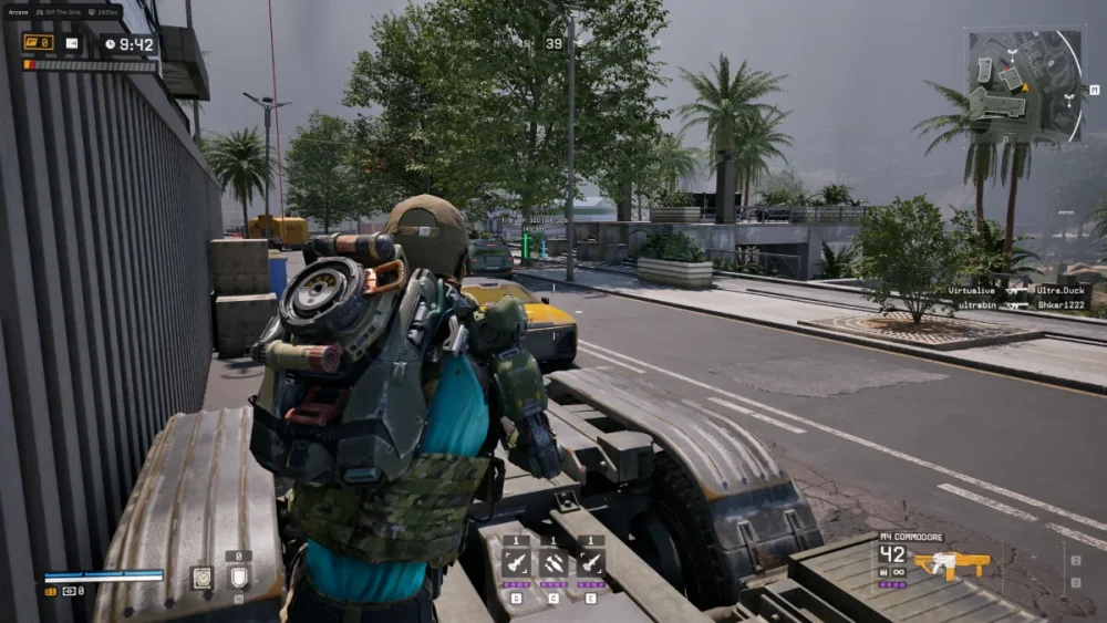 A video game screenshot shows a soldier in tactical gear standing on a vehicle in an urban street. Palms and buildings are visible. The mood is tense.